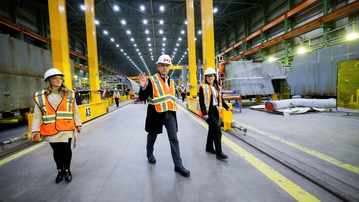 Mark Carney marche en habit de protection dans un entrepôt.