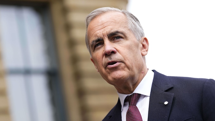 Gros plan de Mark Carney, le regard attentif et le visage grave, vêtu d'un veston foncé et d'une cravate.