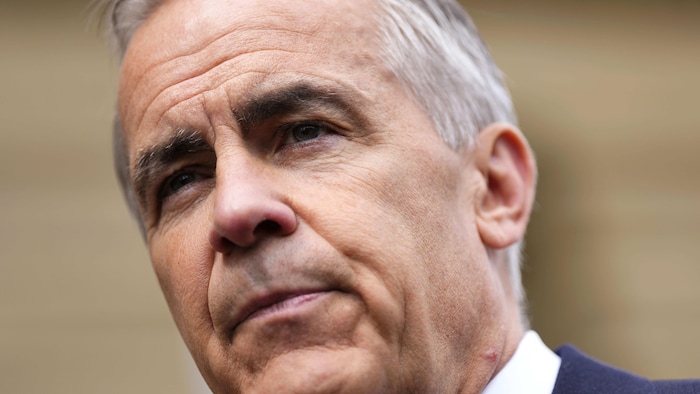 Gros plan sur Mark Carney, le regard attentif et le visage grave, vêtu d'un veston foncé.