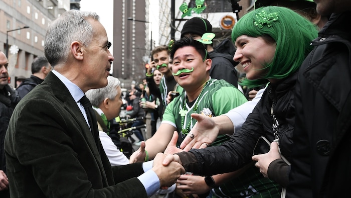 Mark Carney salue avec effusion des participants costumés au défilé de la Saint-Patrick.
