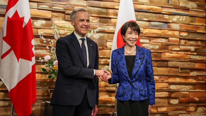 Mark Carney et Sanae Takaichi se serrent la main en souriant.