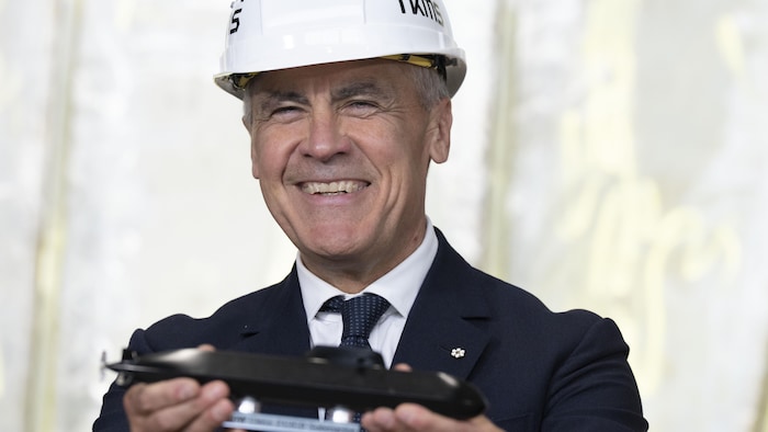 Le premier ministre Mark Carney brandit une maquette de sous-marin lors de sa visite des installations de Thyssenkrupp Marine Systems (TKMS) à Kiel, en Allemagne, le 26 août 2025.