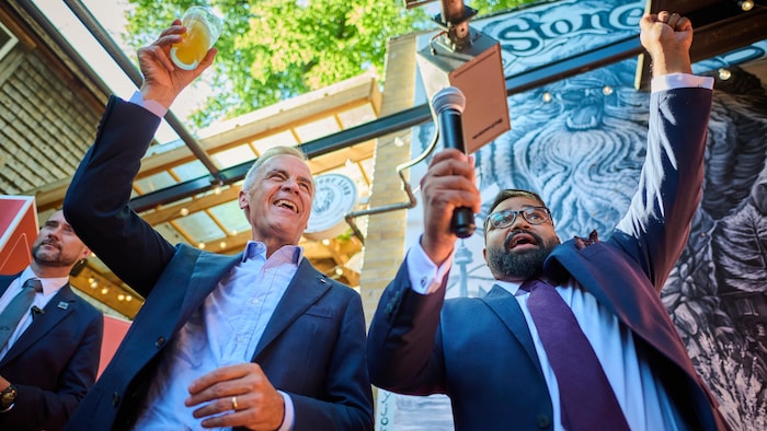 Mark Carney (à gauche) et Tanveer Shahnawaz célèbrent avec des sympathisants au pub The Stone Lion à Toronto, le mercredi 5 août 2026.