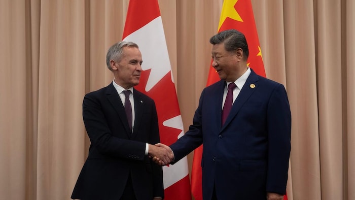 Mark Carney serre la main de Xi Jinping devant des drapeaux canadiens et chinois.