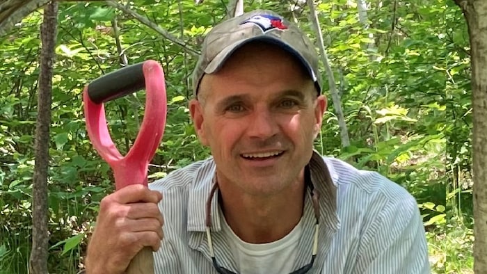 Mark Kuhlberg avec une pelle et un chapeau devant une forêt.