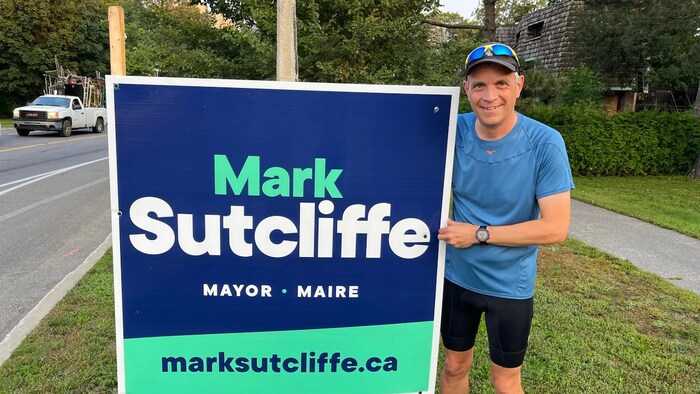 Mark Sutcliffe à côté d'une de ses pancartes électorales.