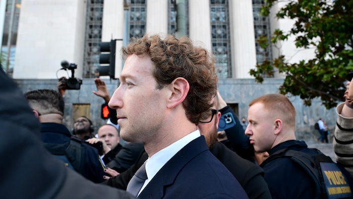 Il est entouré de nombreuses personnes, dont des photographes.
