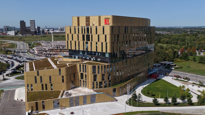 Le campus de 10 étages vu des airs. Il est entouré de routes passantes, de verdure et est situé dans un quartier en développement.