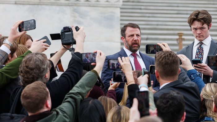Markwayne Mullin, sur les marches du Capitole, est entouré de journalistes qui lèvent leurs téléphones vers lui. 