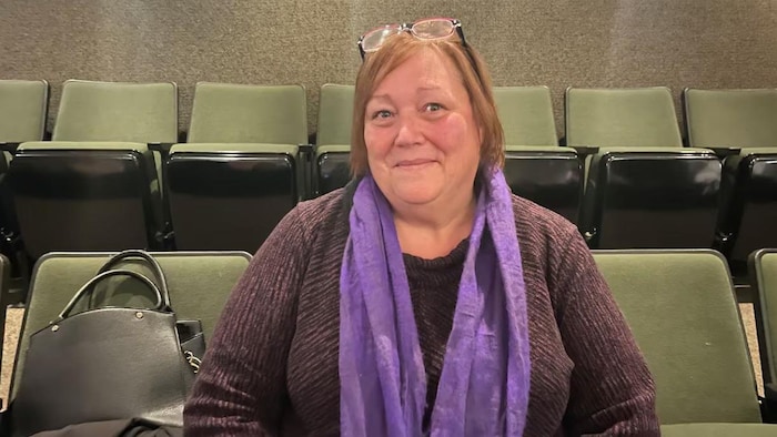 Une femme souriante assise dans une salle.