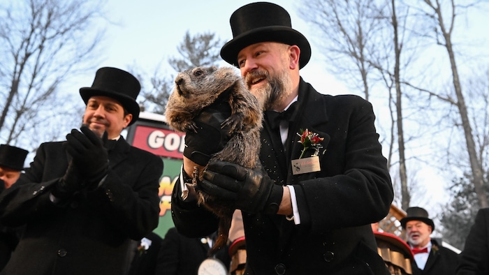 Un homme portant un haut de forme tient fièrement une marmotte.