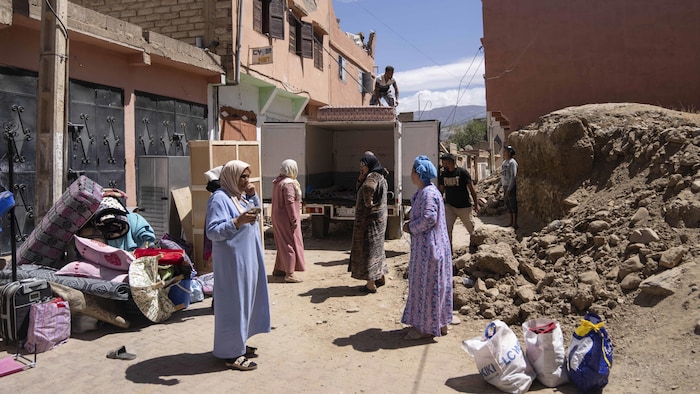 Des femmes sont postées près d'un camion, entourées de sacs et de biens divers, au milieu des décombres.
