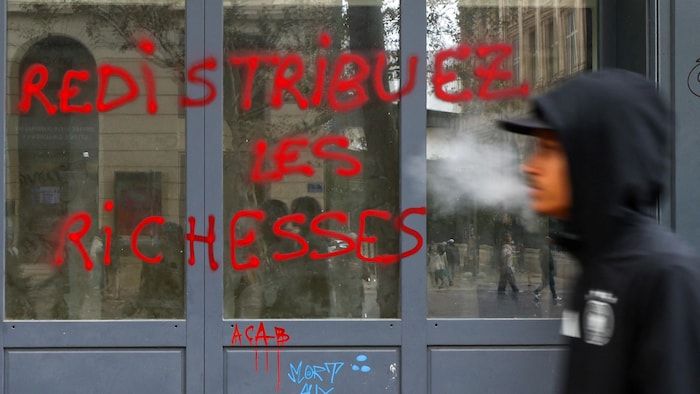 Un homme passe devant un graffiti sur lequel on peut lire « Redistribuer les richesses », peint sur la vitrine d'un magasin, au lendemain des affrontements survenus lors d'une journée nationale de manifestations contre le coût de la vie et la hausse des prix des carburants, à Marseille, en France, le 18 octobre 2026.