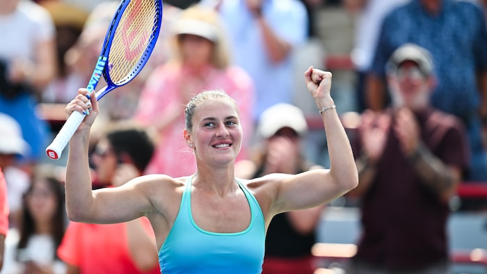 Une joueuse de tennis sourit, les bras dans les airs.