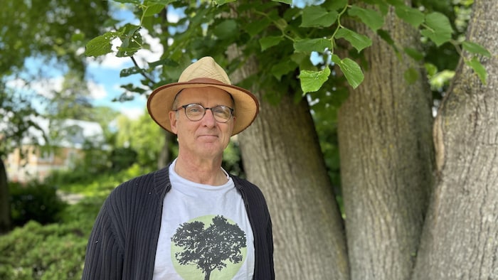 Un homme pose devant un arbre. 