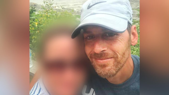 Martin Carpentier porte une casquette blanche de marque Nike. Il a une petite barbe aux teintes de roux, les cheveux bruns ainsi que les yeux bruns.