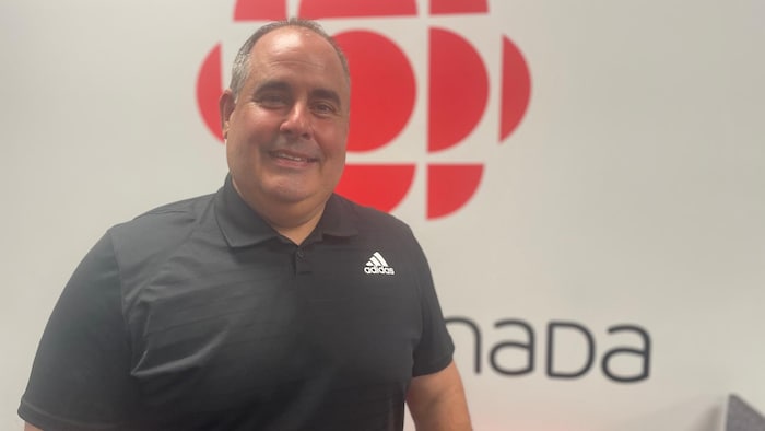 Martin Ferron sourit pour la caméra devant le logo de Radio-Canada.