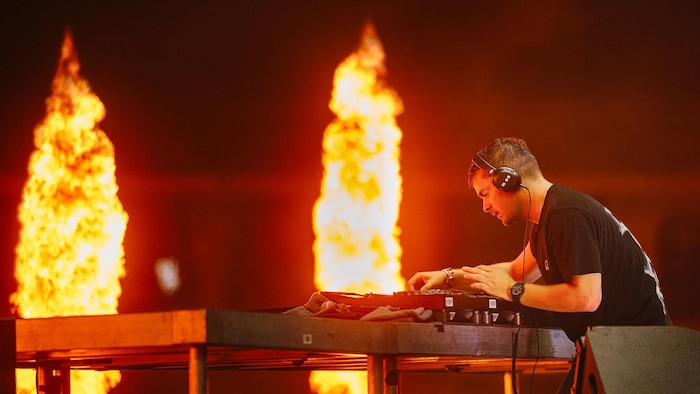 Martin Garrix ajuste ses platines sur scène devant des jets de flammes.