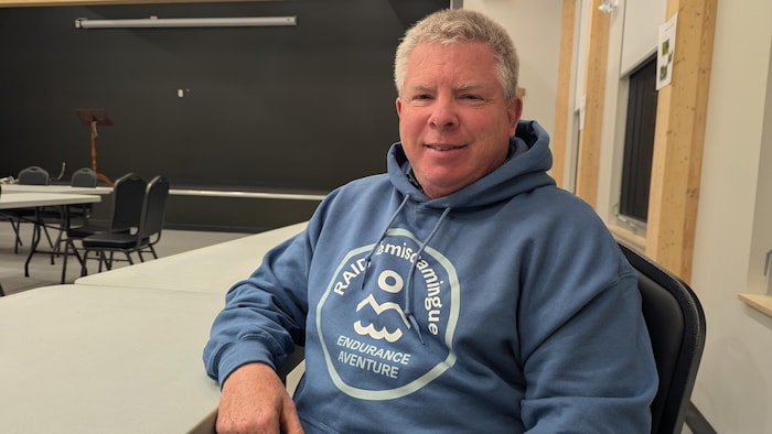 Martin Lefebvre pose dans un centre communautaire après un conseil de la MRC, il porte un chandail chaud à l'effigie du Raid Témiscamingue.