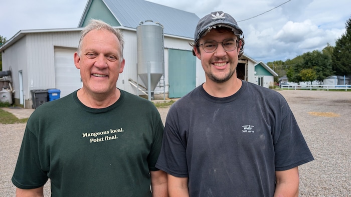 Deux hommes souriants regardent la caméra, en arrière-plan un bâtiment agricole