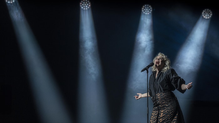 Sur une scène de spectacle, Martine St-Clair chante à un micro, les bras ouverts.
