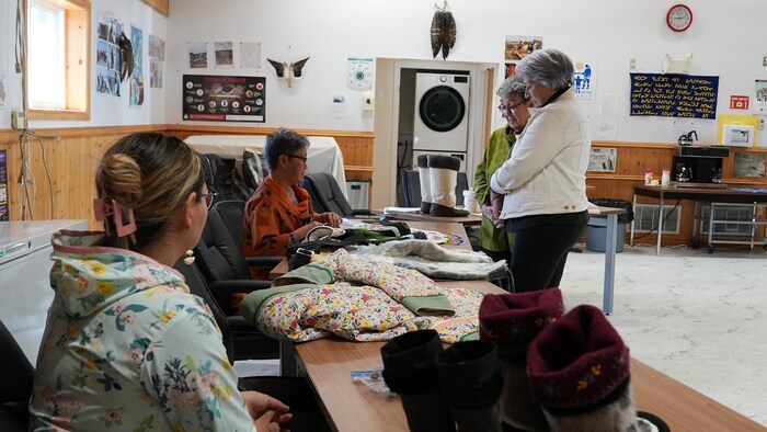 Des femmes assises derrière une table montrent des parkas traditionnels à la gouverneure générale du Canada, Mary Simon, au Centre Tukisigiarvik, à Iqaluit, au Nunavut, le 7 juillet 2025.