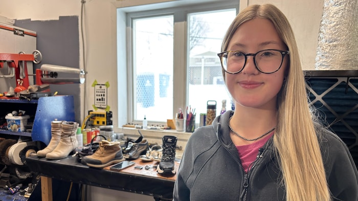 Une jeune femme se tient devant un établi de réparation de souliers.