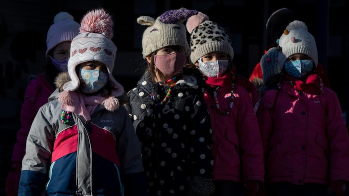 Children in winter gear are wearing face masks.
