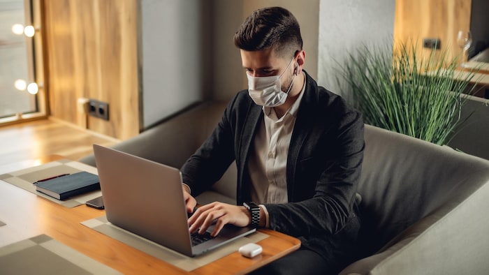 Un homme se sert de son ordinateur portable en portant un masque chirurgical.