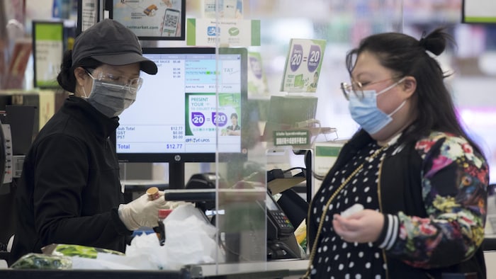 Une caissière et une cliente portent un masque à l'épicerie.
