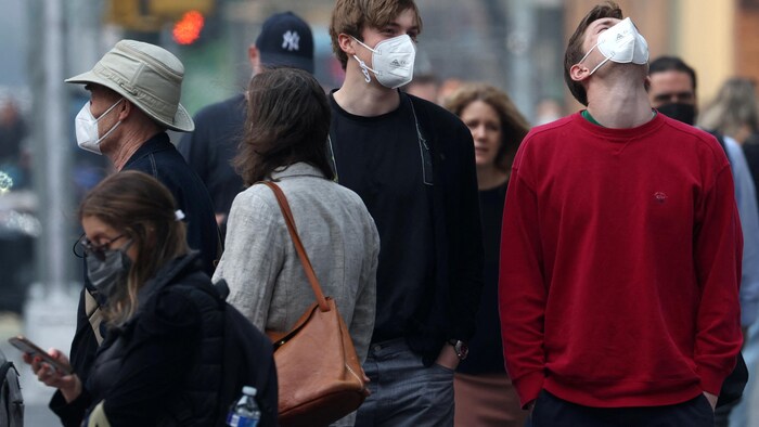 Des gens marchent dans la rue en portant tous un masque.
