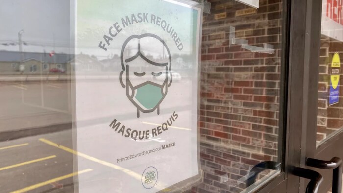 Une affiche sur la porte d'un commerce indique qu'il faut porter un masque pour entrer.