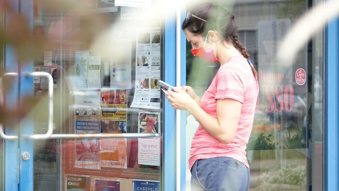 Une femme portant un masque consulte son téléphone intelligent à l'entrée d'un commerce.