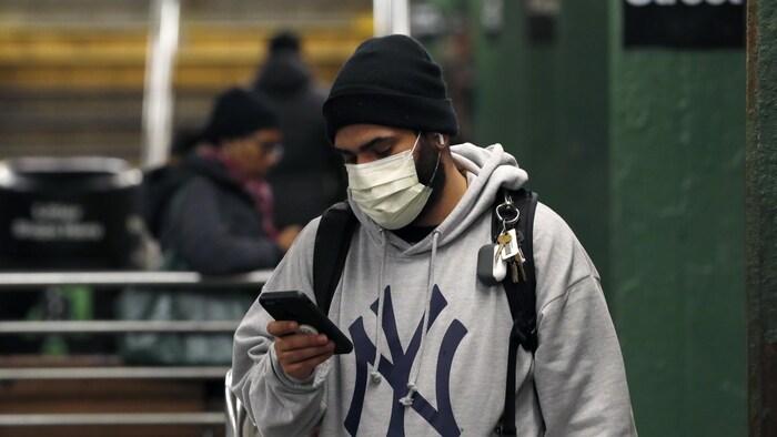 Un homme porte un masque sanitaire et consulte son téléphone mobile dans le métro de New York. 