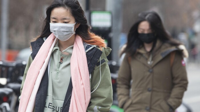 Deux femmes portent un masque chirurgical en marchant dans la rue à Toronto.