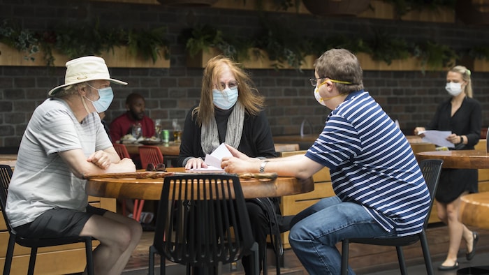 Trois clients portant un masque sont assis à une table.