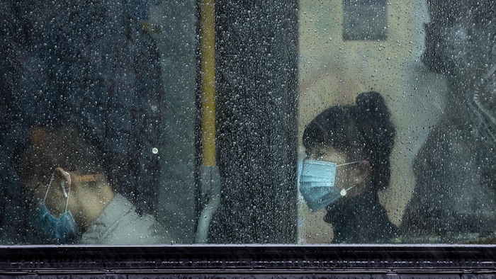 Des gens,que l'on aperçoit à travers une fenêtre embuée par la pluie, portent un masque dans un autobus de Vancouver. 