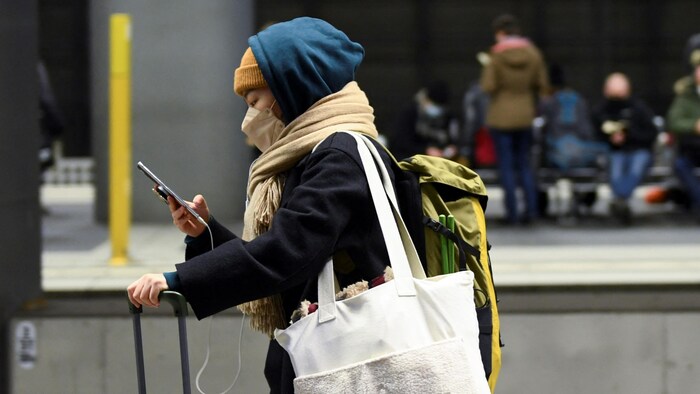 Une personne vêtue d'une tuque, d'un masque et d'un capuchon, regarde son téléphone en poussant sa valise devant elle à Berlin, le 22 décembre 2021.