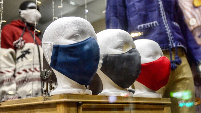Des mannequins portent des masques en tissu dans la vitrine d'une boutique.
