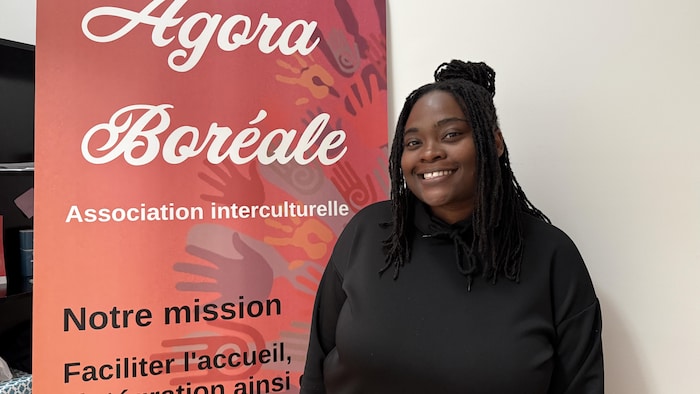 Sabine Dasemé pose aux côtés d'une affiche de l'Agora Boréale.