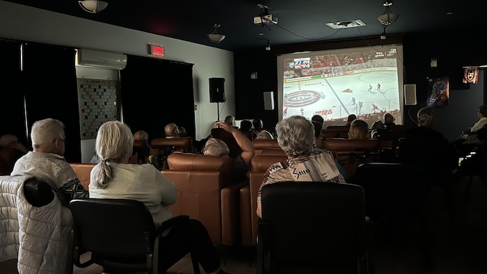 Des personnes âgées assises devant un écran géant.