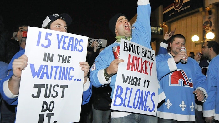 Des partisans vêtus de gilets des Nordiques montrent des pancartes sur lesquelles ils demandent à la LNH de ramener une équipe à Québec. 