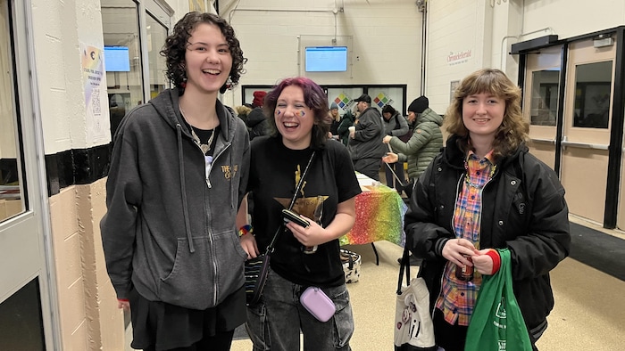 Un groupe de trois jeunes qui sourient ou rient aux éclats dans le couloir d'un aréna.