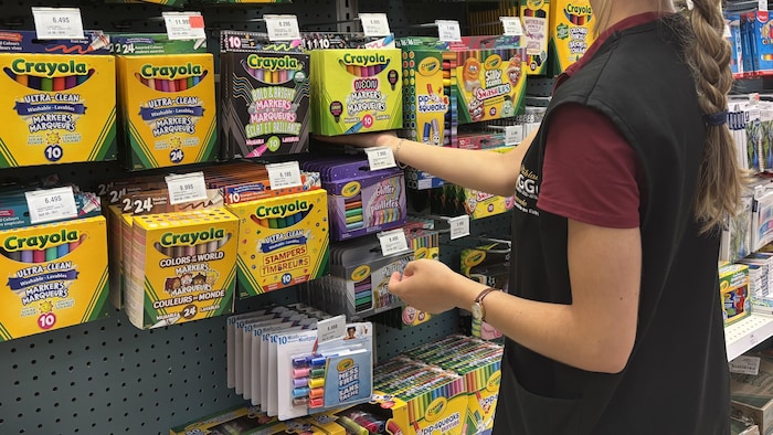 Une employée de la Biblairie GGC range des crayons dans un étalage.