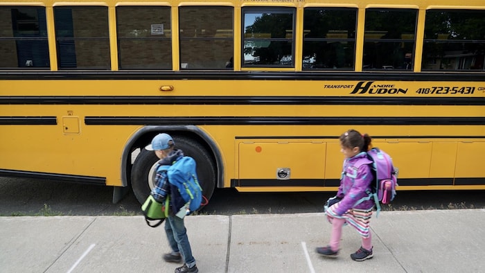 Deux jeunes élèves sortent d'un autobus scolaire.