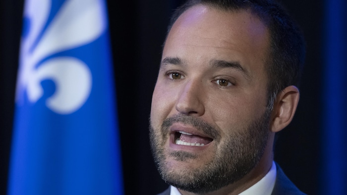 Le ministre s'exprime devant un drapeau du Québec.