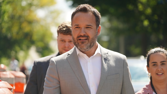 Mathieu Lacombe marche dehors, suivi par deux personnes.