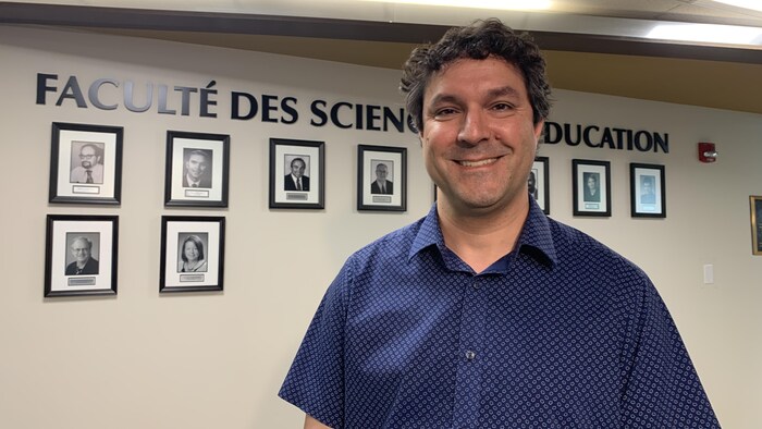 Un homme sourit pour la photo devant un mur de la Faculté des sciences de l'éducation.