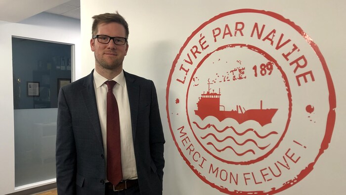 Un homme en complet devant un logo rouge.