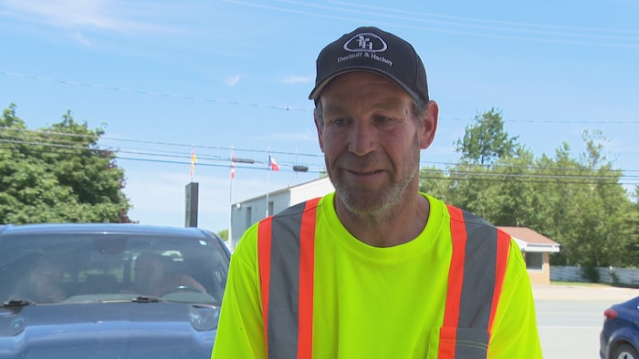 Un homme dehors qui porte une veste jaune et orange réfléchissante et coiffé d'une casquette Thériault & Hachey.